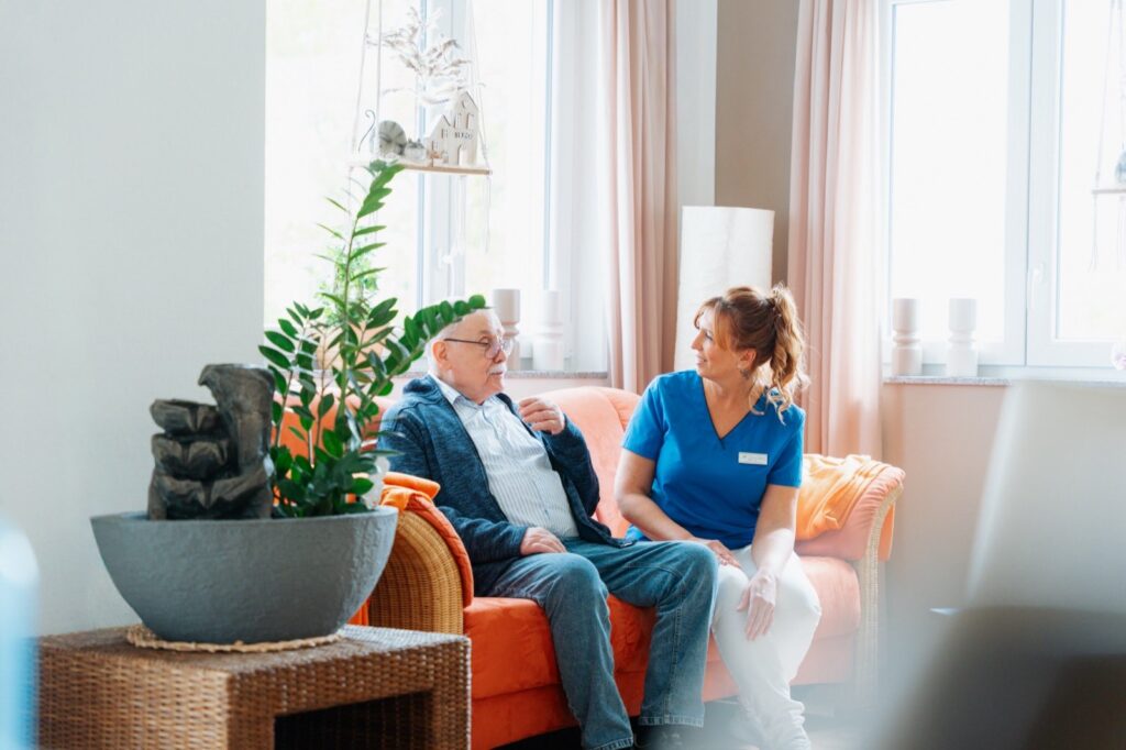 Ein Bewohner und eine Pflegekraft im Gespräch auf einer Couch.